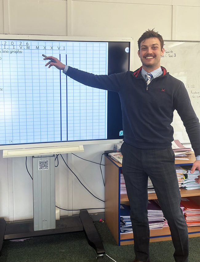 Charlie smiling infront of his whiteboard in the classroom