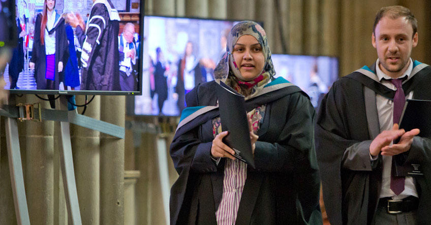 Two graduates standing in front of the screens at Graduation