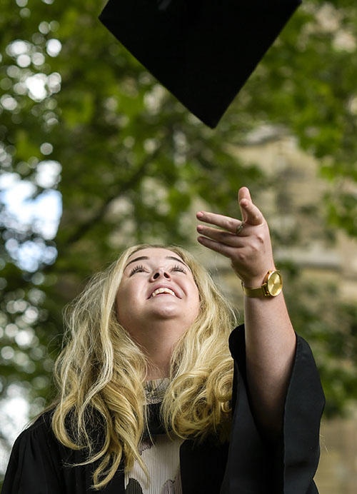a smiling female student is throwing her hat in the air