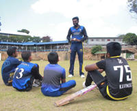 Hemi is teaching cricket in Sri Lanka to several children sitting on the floor