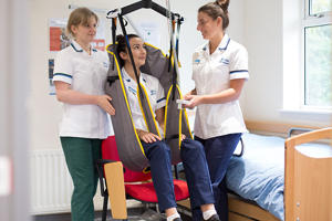 Two students are practising using a hoist which has another student sitting in it.
