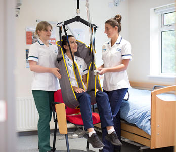 Two students are practising using a hoist which has another student sitting in it.