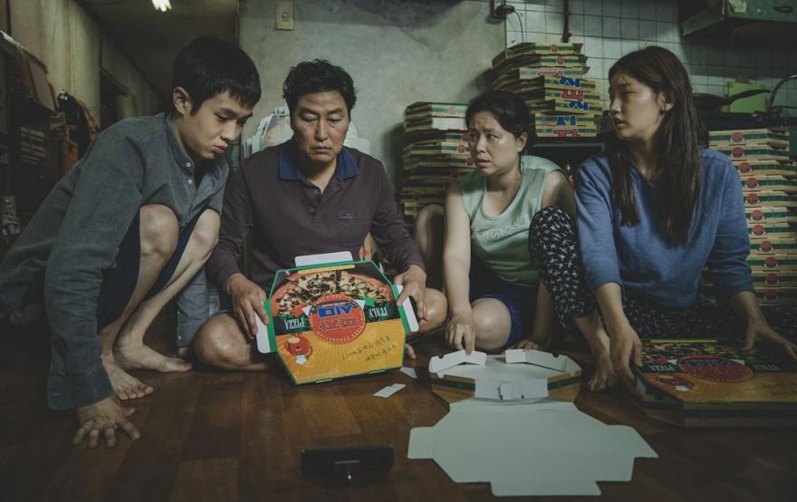 A screen shot from the film "Parasite" featuring a firmly crowded around pizza boxes on the floor