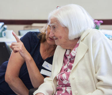 An elderly lady with white hair converses with a friend