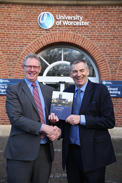 Two men in suits shake hands and pose for a photograph at the University of Worcester