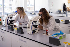 Two female students are looking into microscopes in a lab