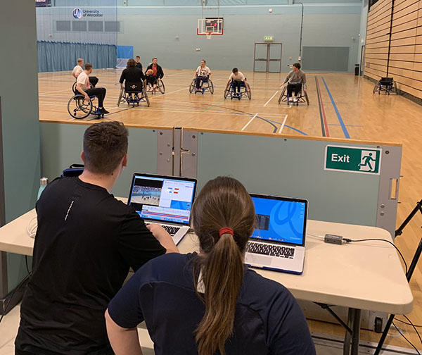 Two colleagues doing sports analysis on a group of players player wheelchair basketball in front of them