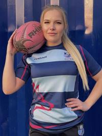 A student holding a rugby ball wearing a rugby kit