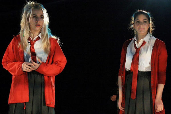 Two girls are on stage dressed in school uniform speaking to each other