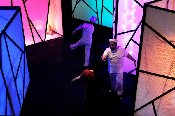 Two people dressed in white are stretching on a brightly coloured stage