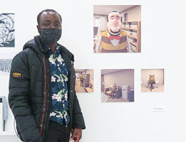 A picture of Tbi standing next to his work. He is wearing a face mask