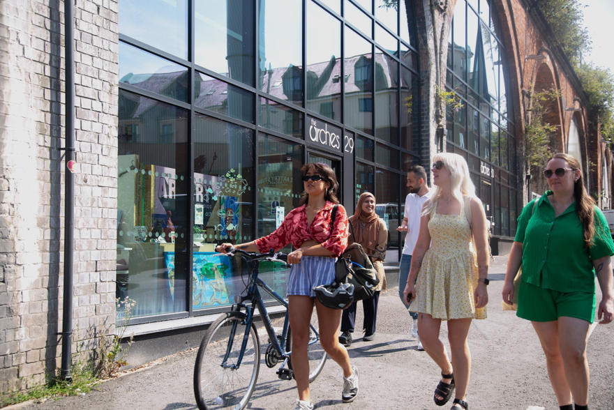 Students walking down a pathway in the city towards the University. One walks with  a bike