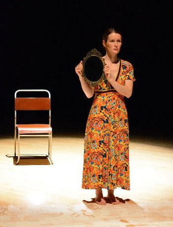 A lady stands on a stage holding a hat