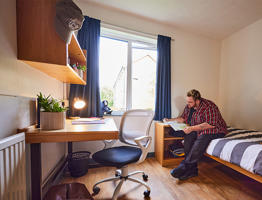 Student reading whilst sat on their bed.