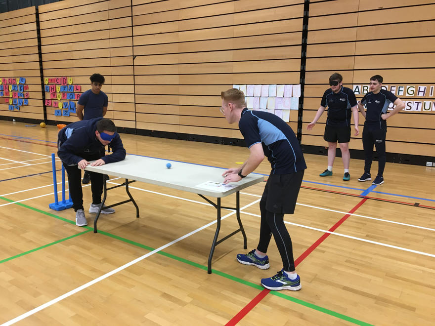 Two people are playing table tennis . One participant is wearing a blindfold