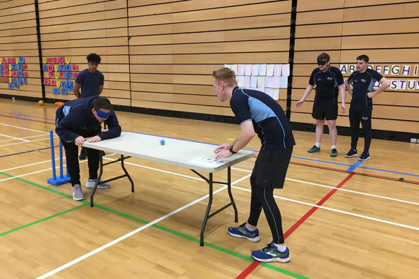Two people are playing table tennis . One participant is wearing a blindfold