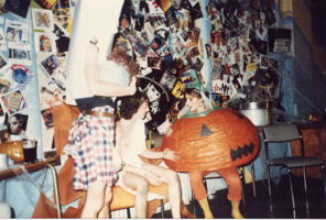 three people in fancy dress, one dressed as a pumpkin, one in a toga and one dressed as a headless man, sit in discussion