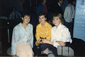 Three women sitting in a nightclub in 1980s clothing