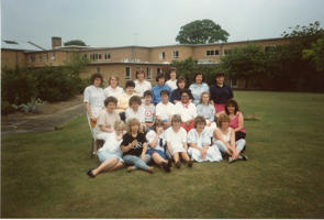 A group of women dressed in 1980s clothing sit in front of a university building