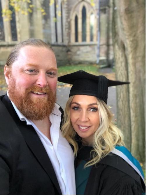 Criminology student in her graduation gown standing in front of Worcester cathedral with a man next to her.
