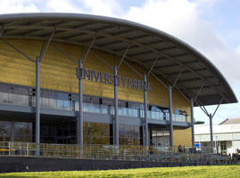 An outside shot of the University arena. It is a gold building with a sloped roof.