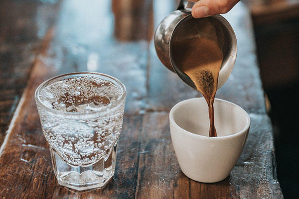 A hand pours coffee into a cup on a table next a glass of water