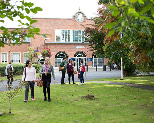 The front of the University at St John's Campus with many happy students walking in front of it