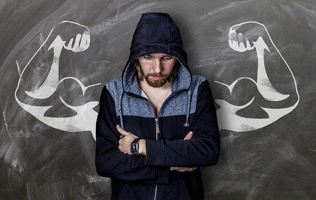 A man is standing in front of a drawing of muscular arms