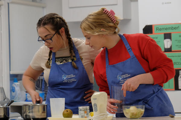 Two students looking at a pot of food cooking