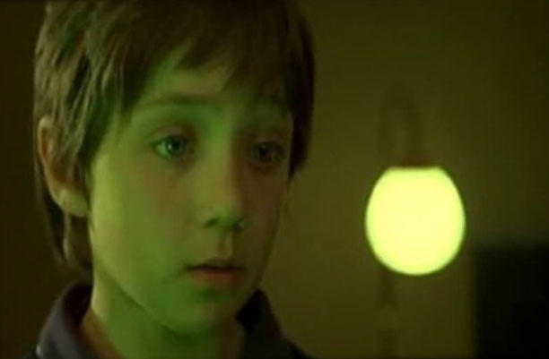 A child is looking intently at something he has a green light shining on him.
