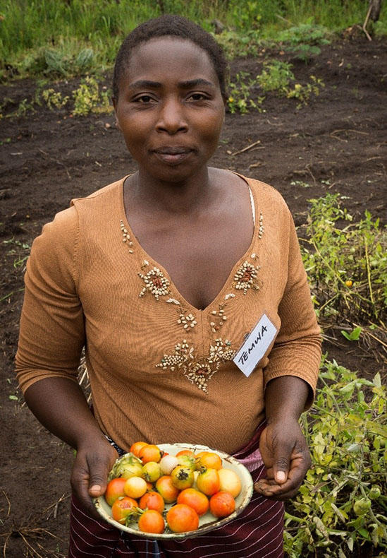 A lady called Temwa is standing in a welt land area holding a tray of fruit