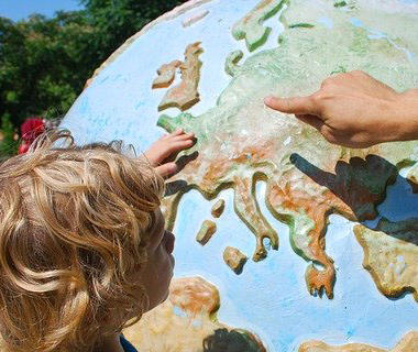 A child is pointing at Europe on a globe