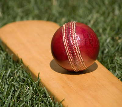 Close up shot of a wooden cricket bat and red ball laid on grass