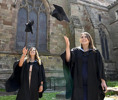 Two female students in graduation robes are smiling and throwing their hats in the air.