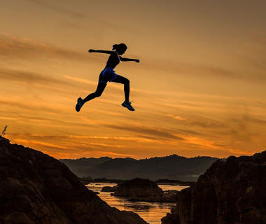 A woman is jumping high in the air during the sunset
