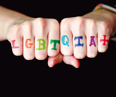 LGBTQ+ written in multiple colours across someone's knuckles
