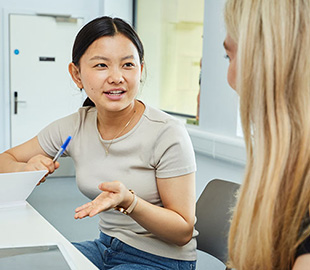 A student talking to another student with a notebook and pen