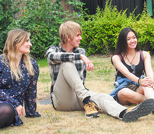 Three students sat on a lawn on campus