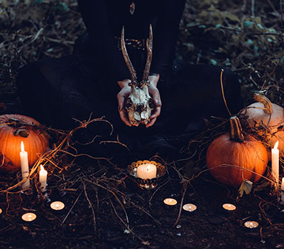 Some hands are holding a skull in candle light next to some pumpkins