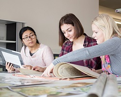three students at a table filled with scrolls and images