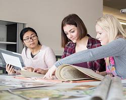 three students at a table filled with scrolls and images