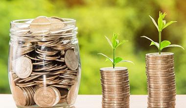 glass jar of coins and two piles of coins with sprouts of plants at the top