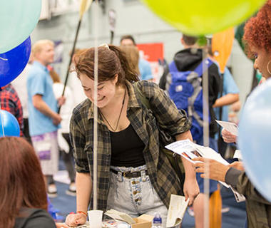 A student is smiling at a welcome event. She is looking over a stall.