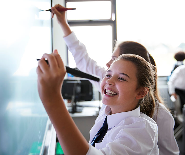 Female high school students wearing uniform using interactive whiteboard during lesson