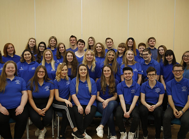 group of students sitting down and wearing blue tops