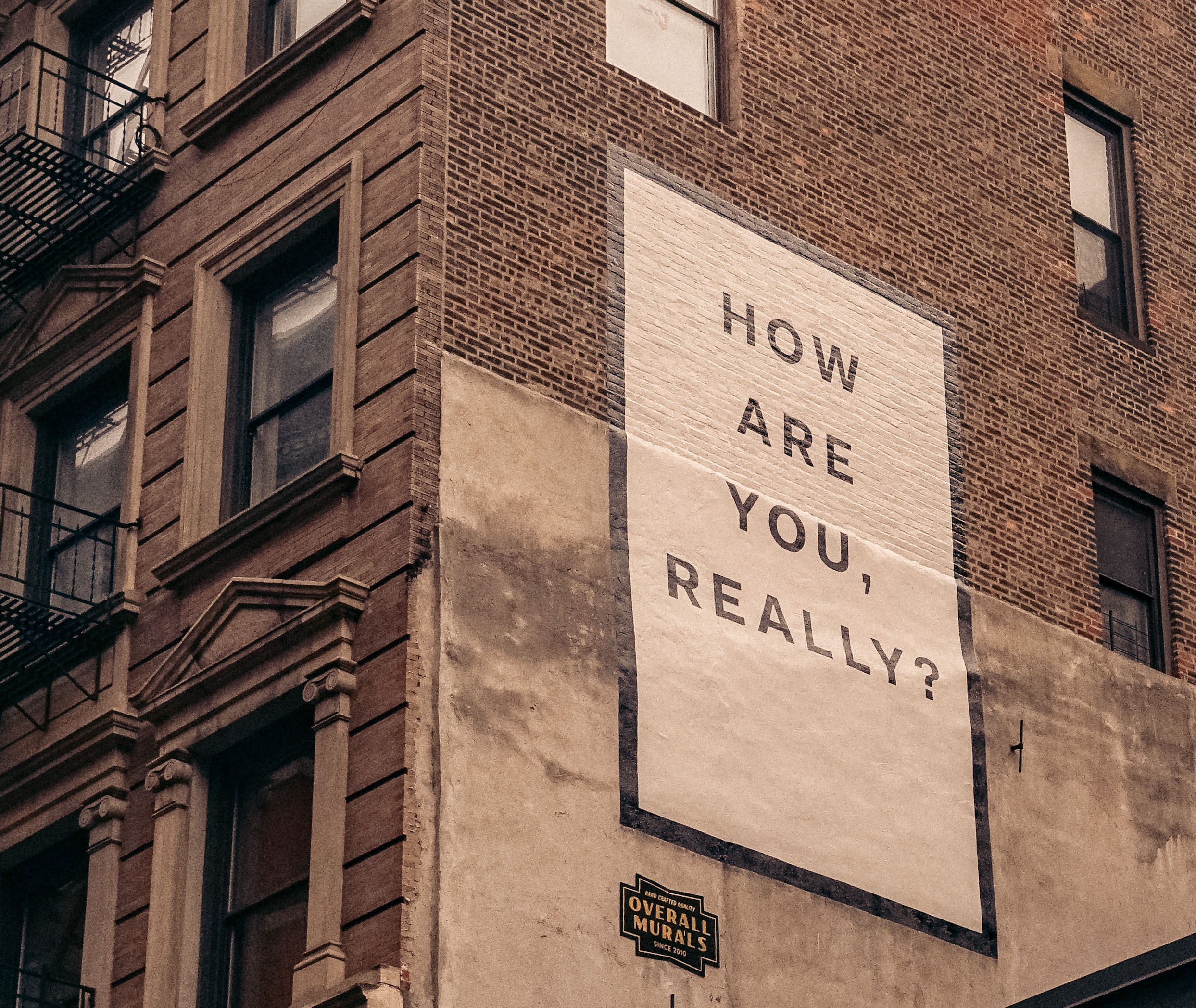 We can see the side of a building which features a sign saying "How are you really?" on it