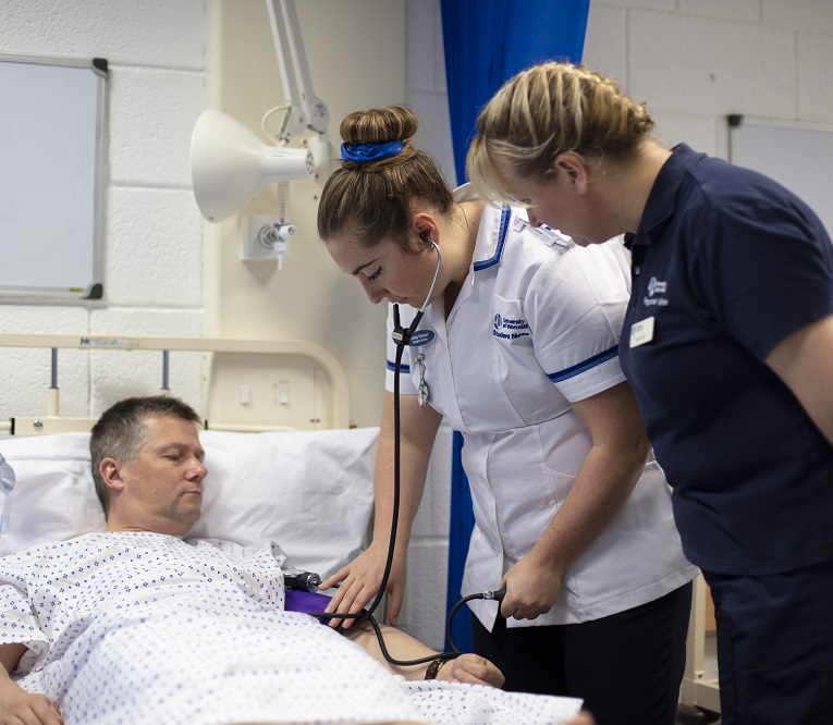 two nurses at the side of the bed in which a patient is lying down