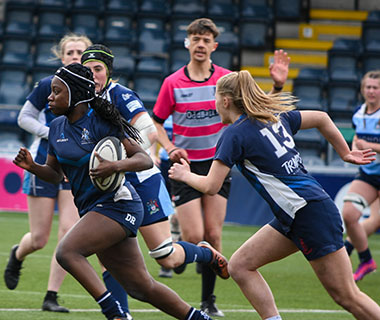 A group of students are running one of them is holding a rugby ball.